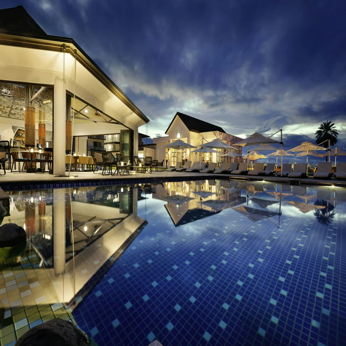 Illuminated outdoor resort pool beside hotel buildings at dusk